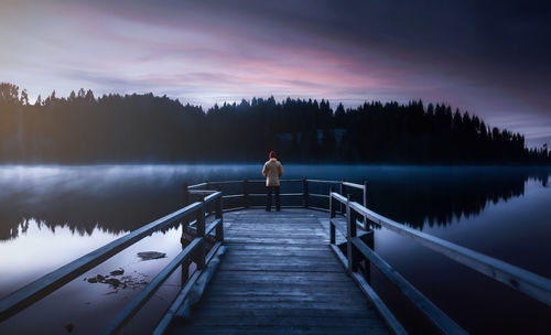 Standing on pier by the foggy lake during sunrise