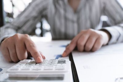 Midsection of businessman calculating with calculator at desk in office