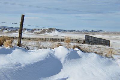 Barbed wire on snow covered field against sky