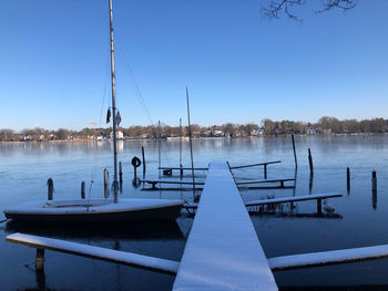 Pier on lake against clear blue sky with boat and snow