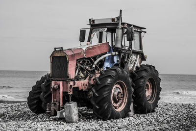 Tractor on field by sea against sky