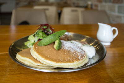 Close-up of pancakes with salad served in plate on wooden table