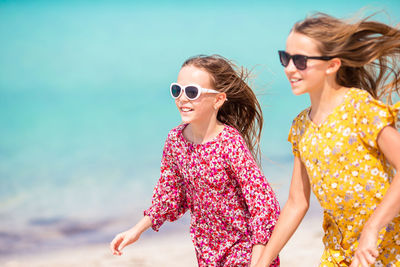 Smiling sisters wearing sunglasses running on beach