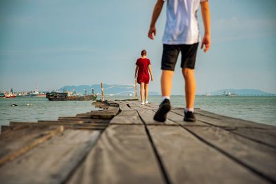 Rear view of people walking on pier by sea against sky