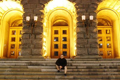 Low angle view of man sitting on staircase of old building at night