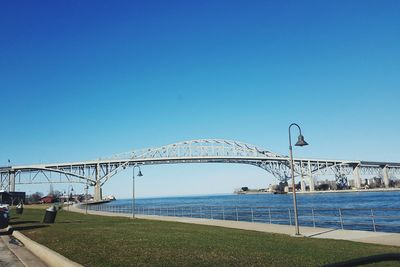 Suspension bridge over sea against clear blue sky