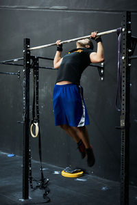 Young man working out doing chin ups in horizontal bar at indoors gym