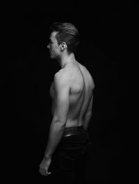 Midsection of shirtless man standing against black background