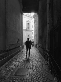 Rear view of man walking on footpath amidst buildings