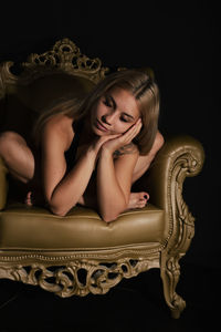 Young woman sitting on sofa against black background