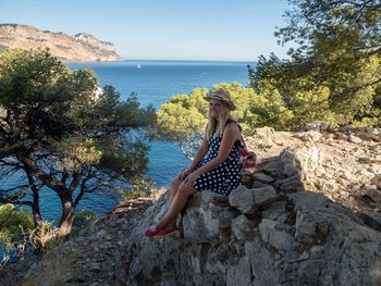 Woman sitting on rock by sea against sky