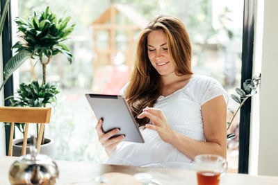 Cute freckled redhead woman is typing in a tablet computer and smiling.