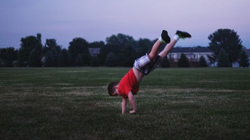 Full length of boy performing handstand on grassy field against sky