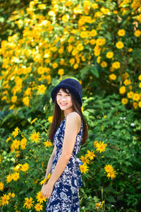 Beautiful young woman standing by yellow flowering plants