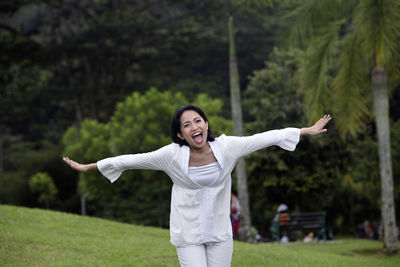 Portrait of happy woman with arms outstretched standing on field at park