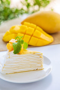 Close up mango crepe cake sliced on a white plate decorated with a piece of mango fruits 