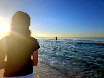 Rear view of woman standing at beach against sky during sunset