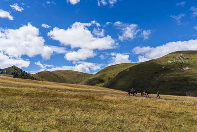 People riding on field by mountain against sky