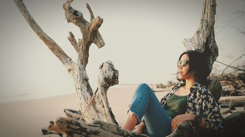 Young woman looking away while sitting on tree trunk