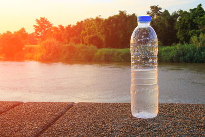 Glass of bottle on lake against trees