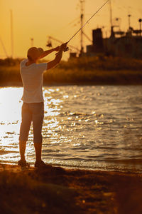 Rear view of woman standing in sea against sky during sunset