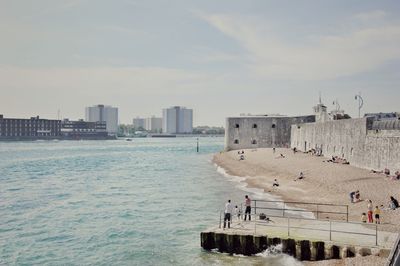 People on beach by buildings against sky