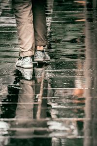 Low section of person standing on wet puddle during rainy season