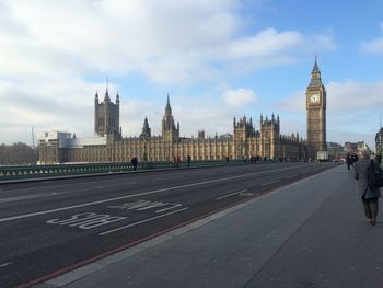 View of palace of westminster from city street against cloudy sky