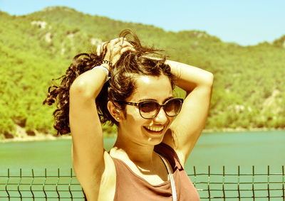 Portrait of smiling young woman tying hair against lake and mountains