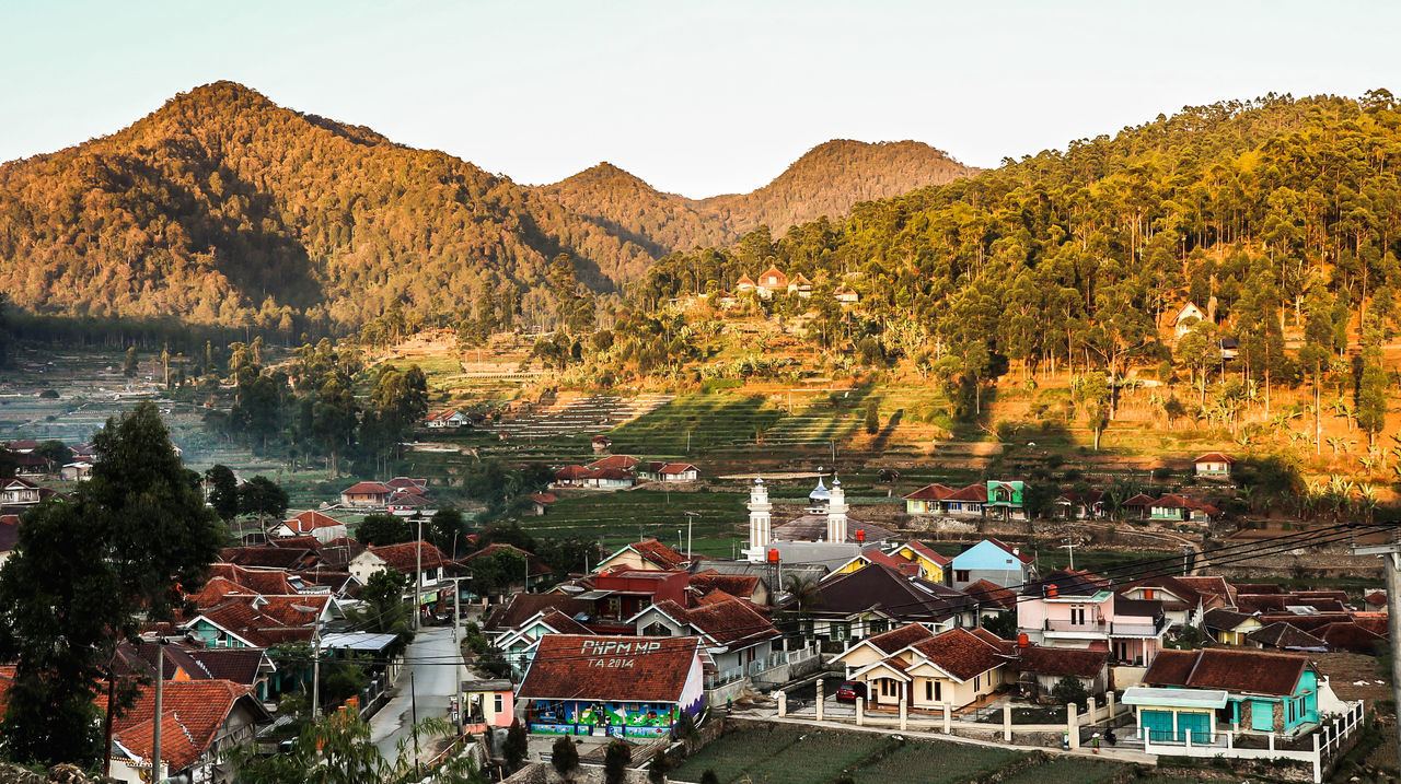 mountain, tree, built structure, architecture, plant, building exterior, residential district, water, no people, nature, beauty in nature, high angle view, sky, building, house, scenics - nature, day, outdoors, growth