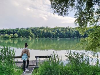 Rear view of man looking at lake against sky