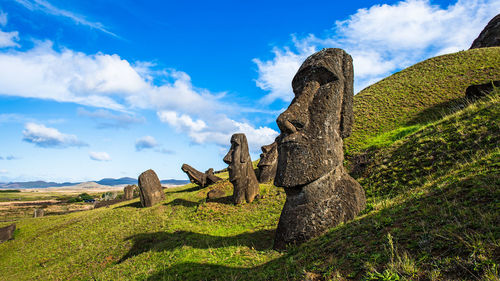 Stone statues on field against cloudy sky