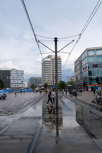 People walking on city street by buildings against sky