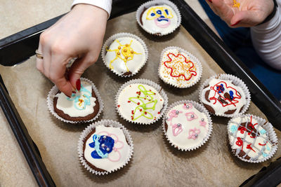 A woman squeezes colored frosting from a tube onto chocolate brown cupcakes covered white frosting.