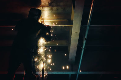 Rear view of silhouette man standing at illuminated staircase