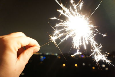 Cropped image of hand holding illuminated sparkler at night