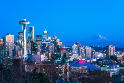 Illuminated buildings in city against clear blue sky