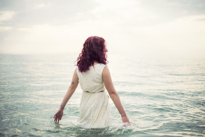 Full length of young woman standing against sea
