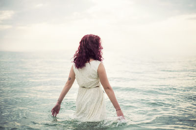 Rear view of young woman in sea against sky