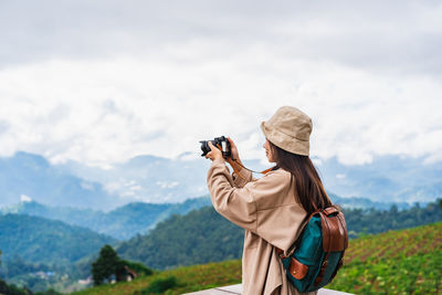 Side view of woman photographing with camera against sky