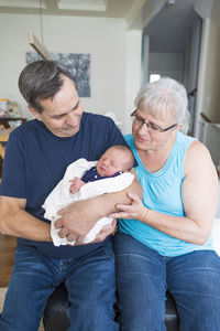 Grandparents with cute newborn granddaughter sitting at home