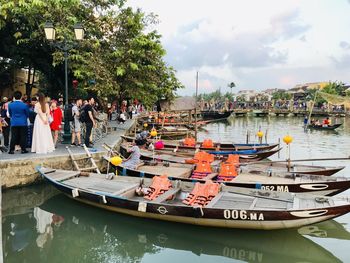 People by boats moored in river