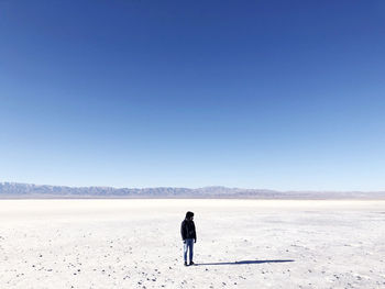 Man standing at salt flat against clear blue sky