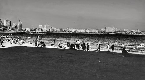 Group of people on beach in city against sky