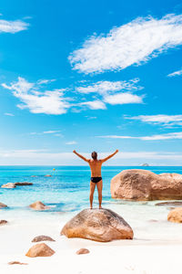 Rear view of woman with arms outstretched on beach against sky