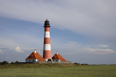 Lighthouse on field by building against sky