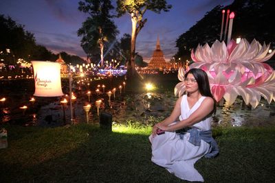 Woman sitting by illuminated built structure against sky