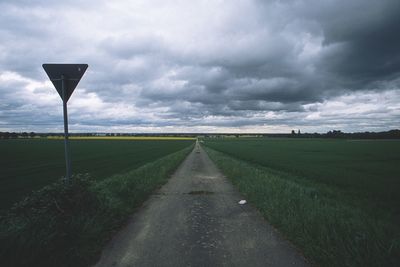 Empty road amidst field against sky