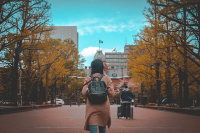 Rear view of woman standing by bare trees in city