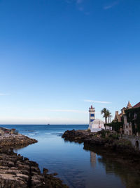 Buildings by sea against clear blue sky